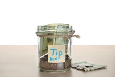Photo of Tip jar and money on wooden table against white background