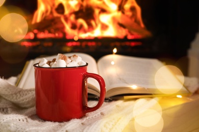 Photo of Cup of cocoa and book on wooden table near fireplace. Cozy Christmas atmosphere