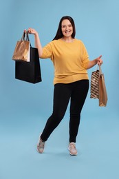 Beautiful overweight woman with shopping bags on turquoise background