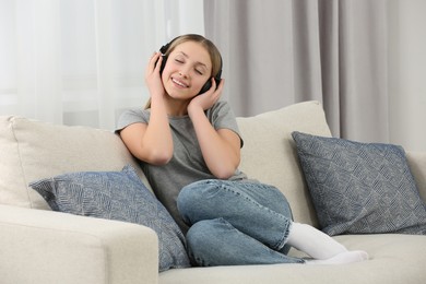Photo of Teenage girl listening to music with headphones on sofa at home