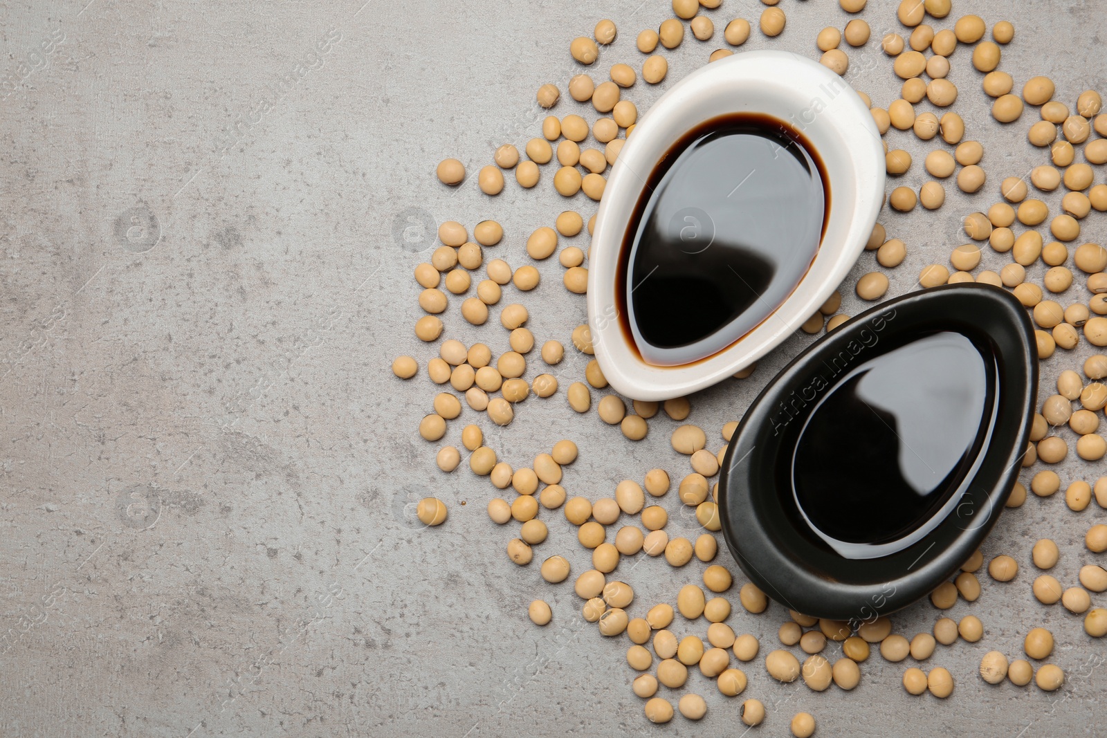 Photo of Dishes of soy sauce and beans on grey background, flat lay. Space for text