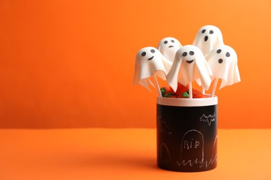 Delicious ghost shaped cake pops on orange background, space for text. Halloween celebration