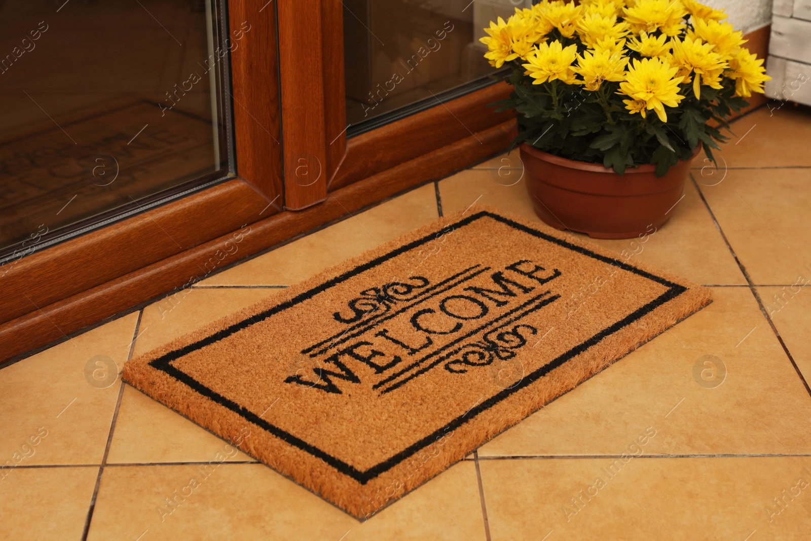 Photo of Door mat with word Welcome and beautiful flowers on floor near entrance