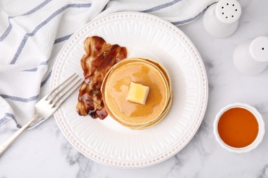 Photo of Delicious pancakes with butter, maple syrup and fried bacon served on white marble table, flat lay