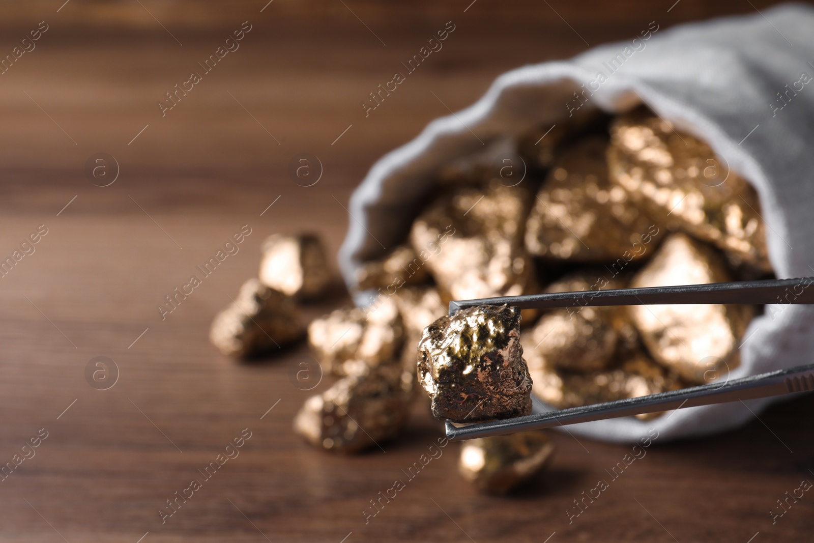 Photo of Tweezers with gold nugget on blurred background, closeup. Space for text