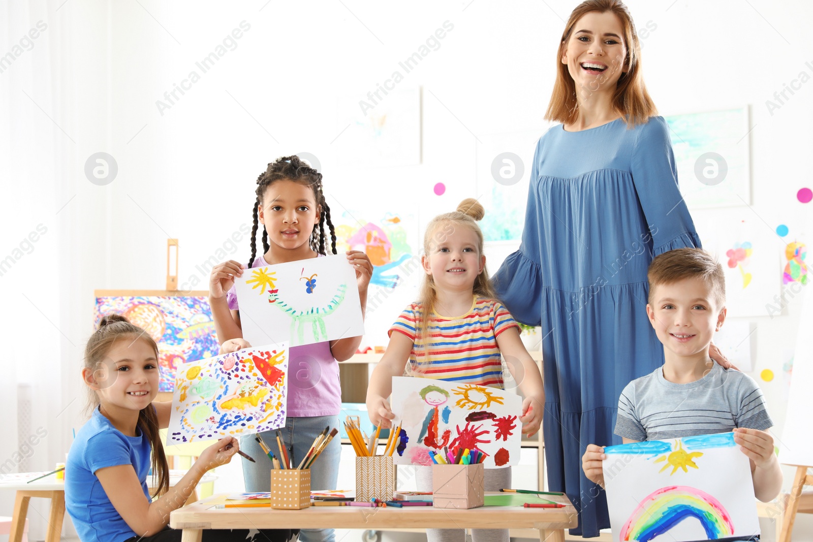 Photo of Cute little children with teacher showing their paintings at lesson indoors