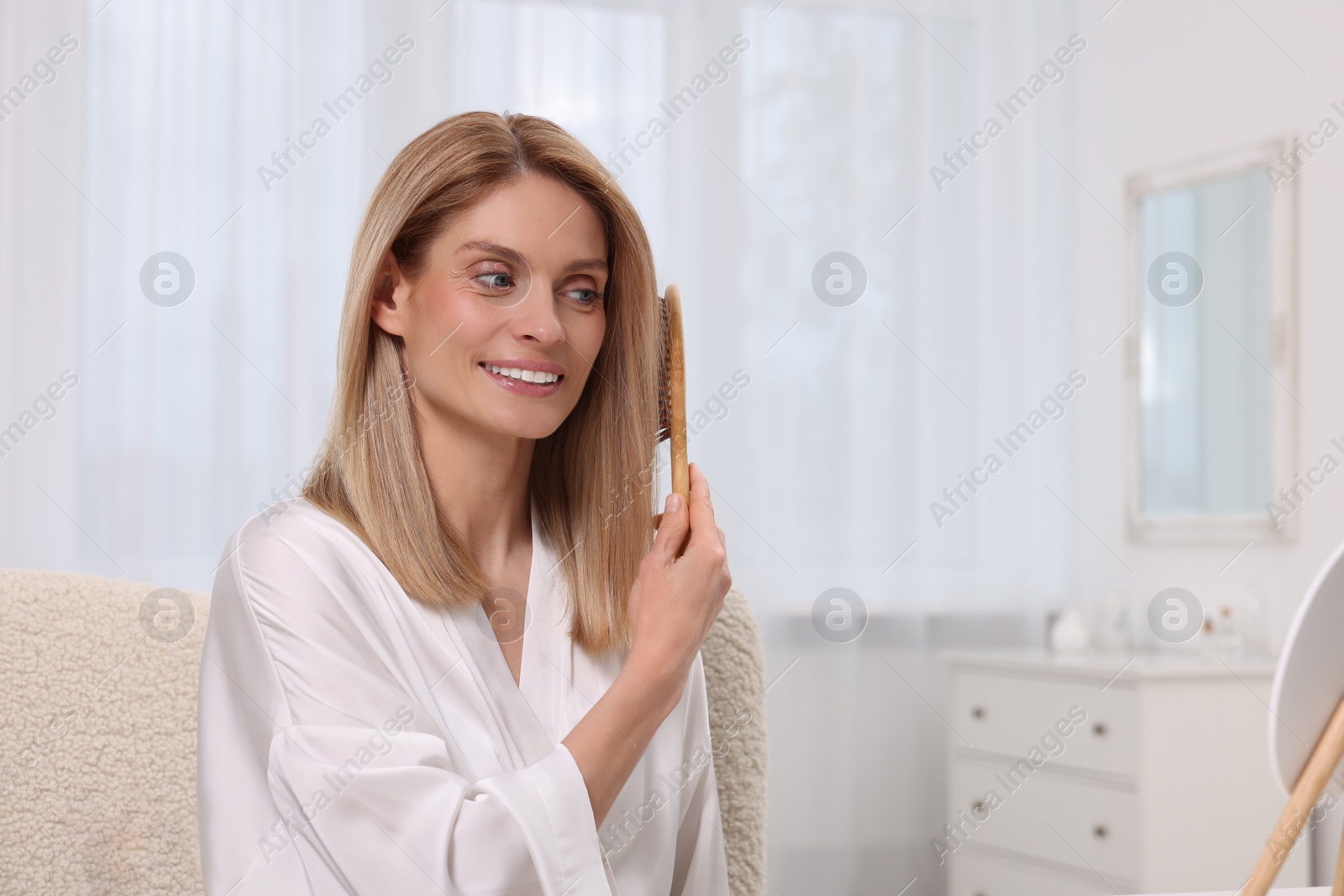 Photo of Beautiful woman brushing her hair near mirror in bedroom. Space for text
