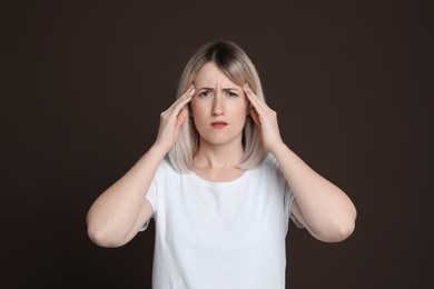 Photo of Woman suffering from headache on dark brown background