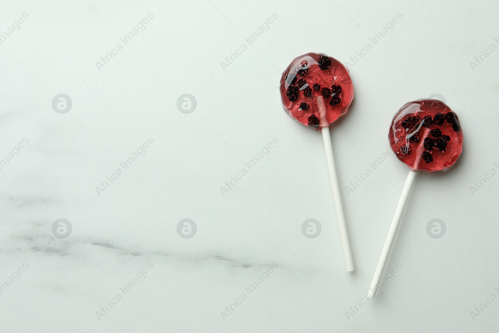 Photo of Sweet colorful lollipops with berries on white marble table, flat lay. Space for text