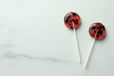 Photo of Sweet colorful lollipops with berries on white marble table, flat lay. Space for text