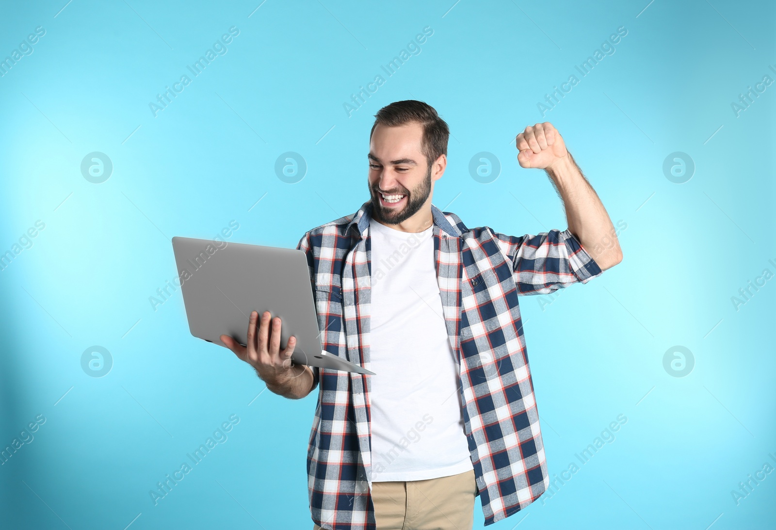 Photo of Emotional young man with laptop celebrating victory on color background