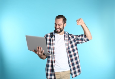 Emotional young man with laptop celebrating victory on color background