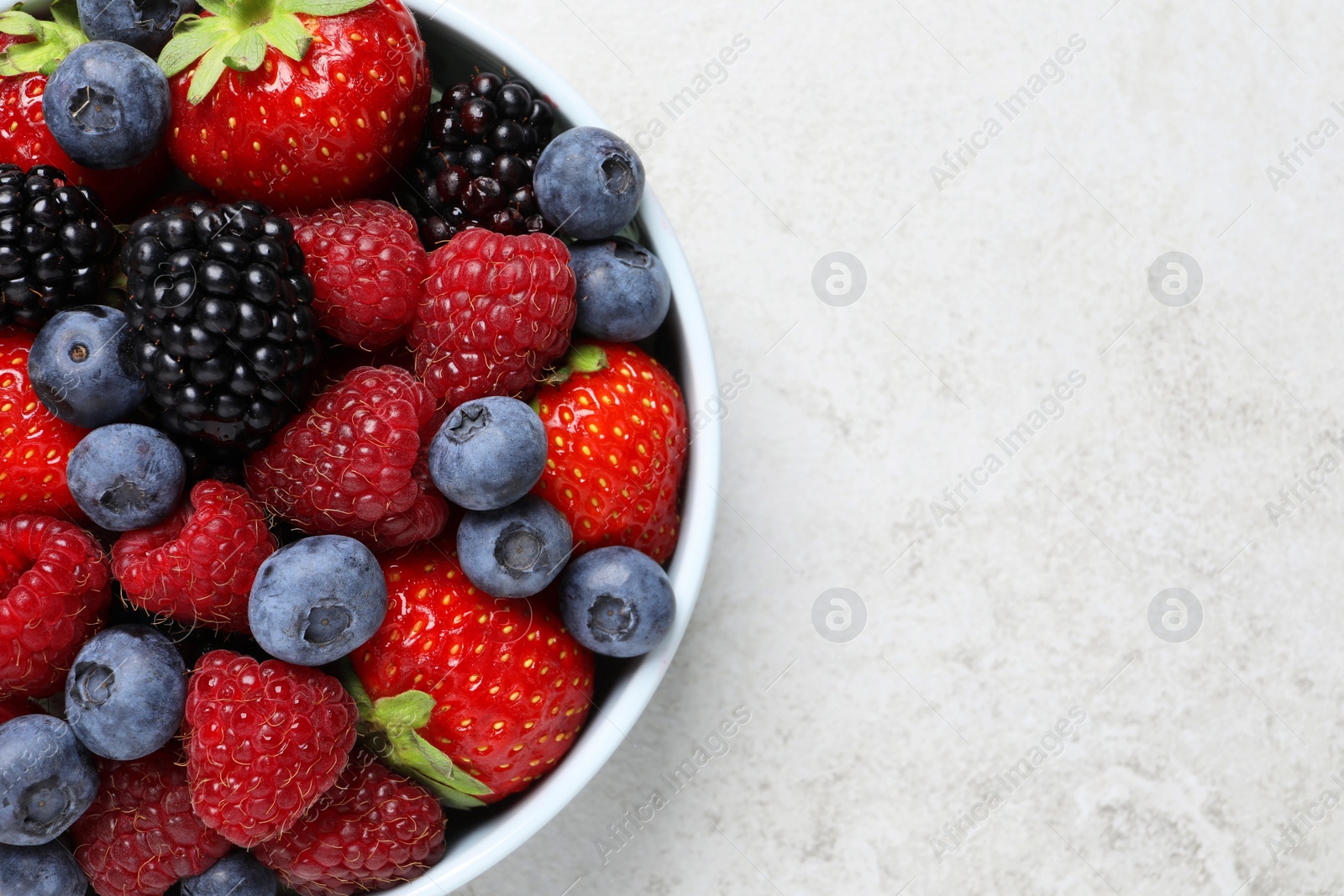 Photo of Many different fresh ripe berries in bowl on light grey table, top view. Space for text