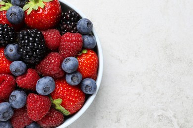 Photo of Many different fresh ripe berries in bowl on light grey table, top view. Space for text