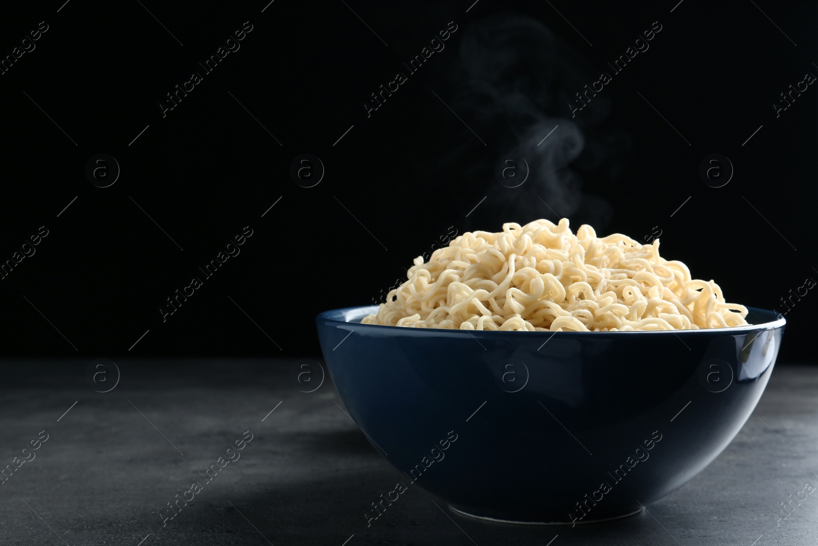 Photo of Bowl of hot noodles on table against black background. Space for text