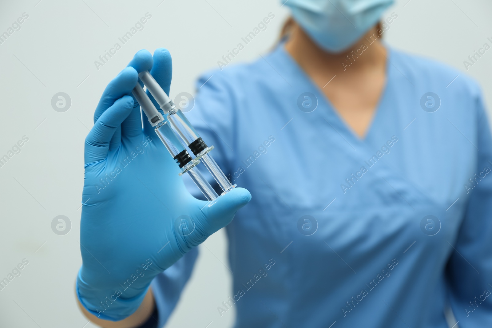 Photo of Doctor holding syringes with COVID-19 vaccine on light background, closeup