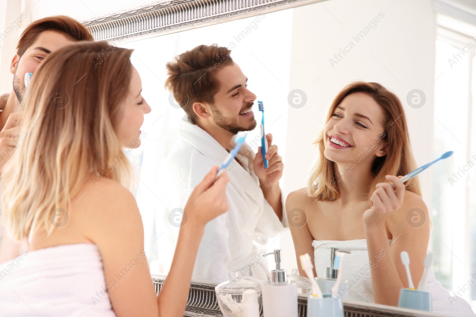 Photo of Young couple with toothbrushes near mirror in bathroom. Personal hygiene