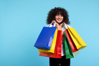 Happy young woman with shopping bags on light blue background