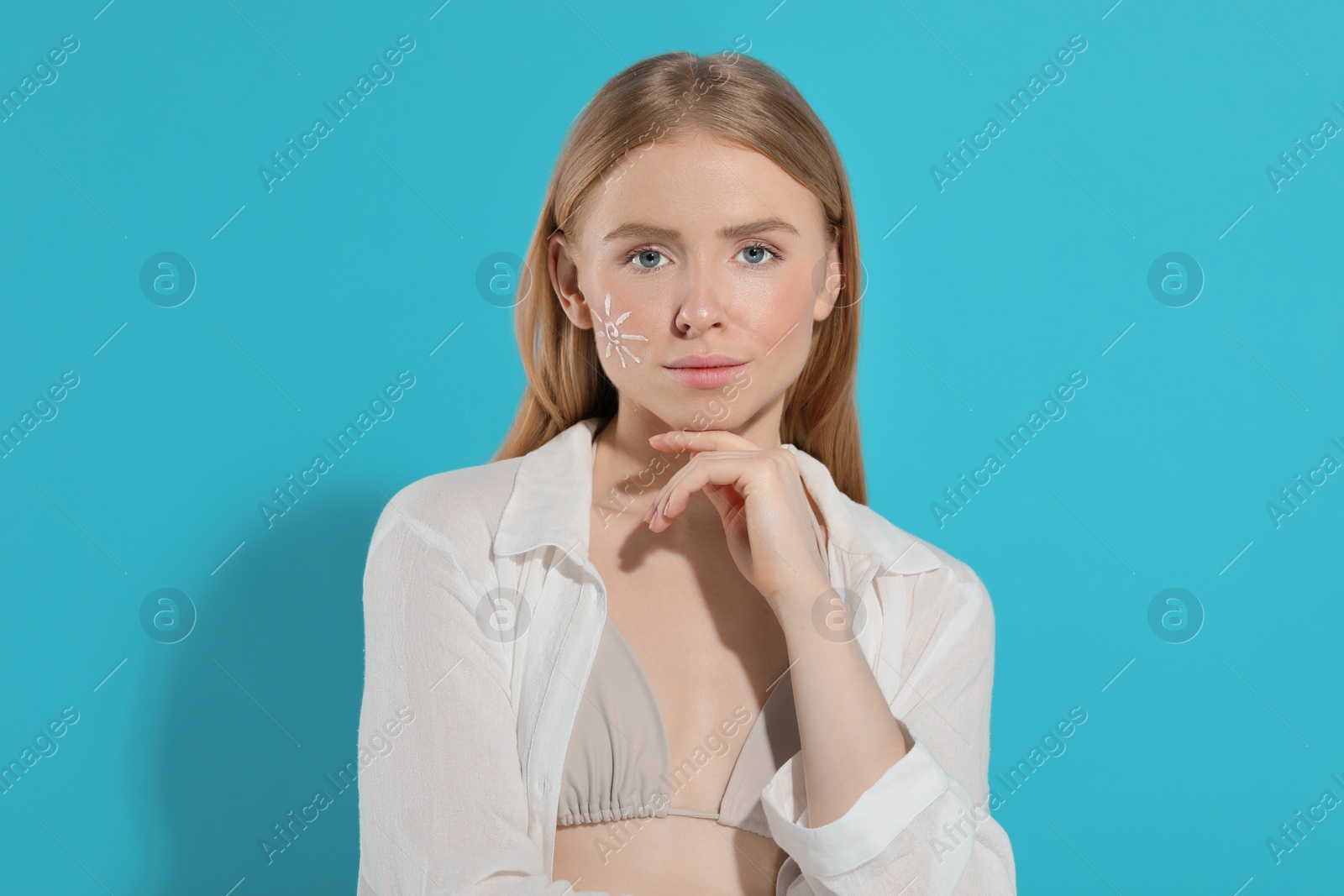 Photo of Beautiful young woman with sun protection cream on her face against light blue background