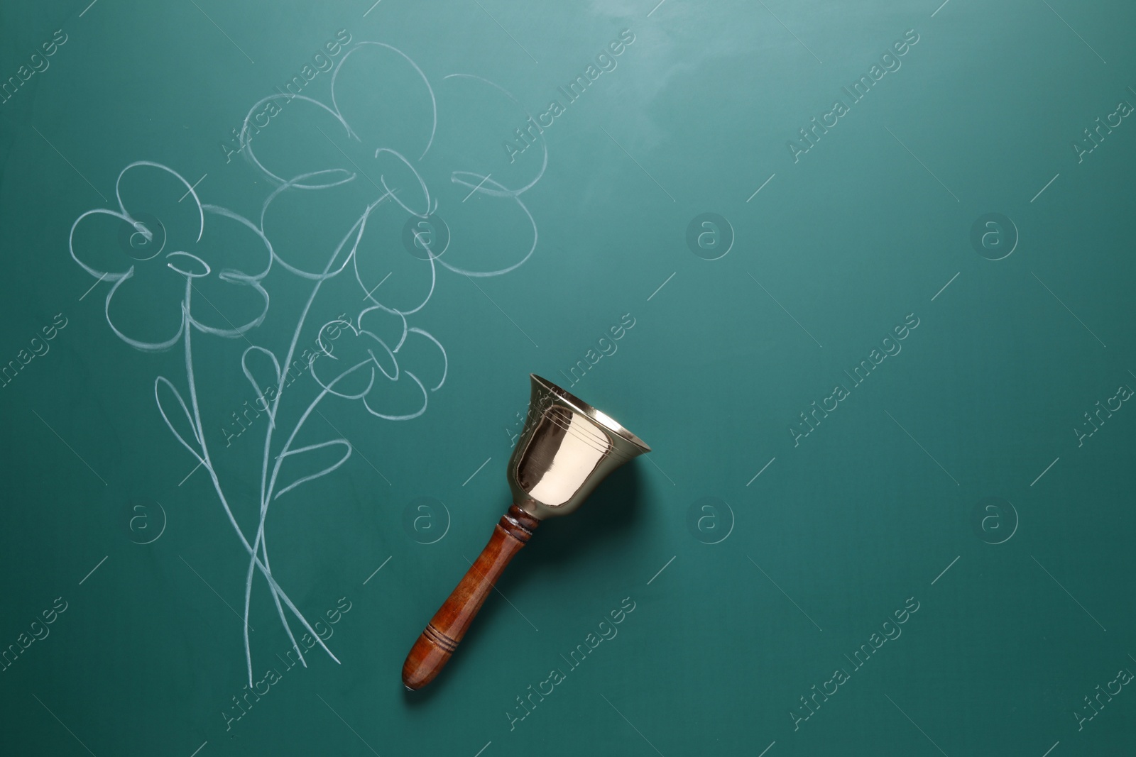 Photo of Golden bell and drawn flowers on green chalkboard, top view. School days