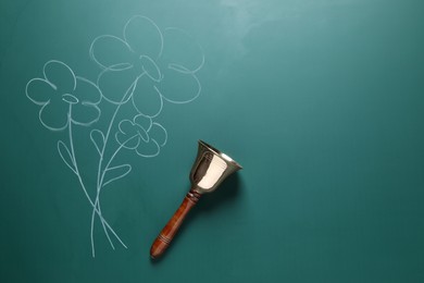 Photo of Golden bell and drawn flowers on green chalkboard, top view. School days