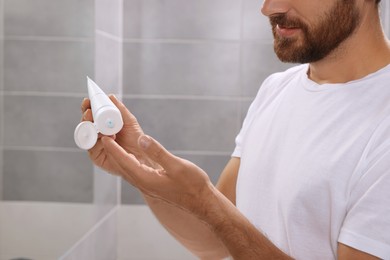 Photo of Handsome man with tube of cream in bathroom, closeup