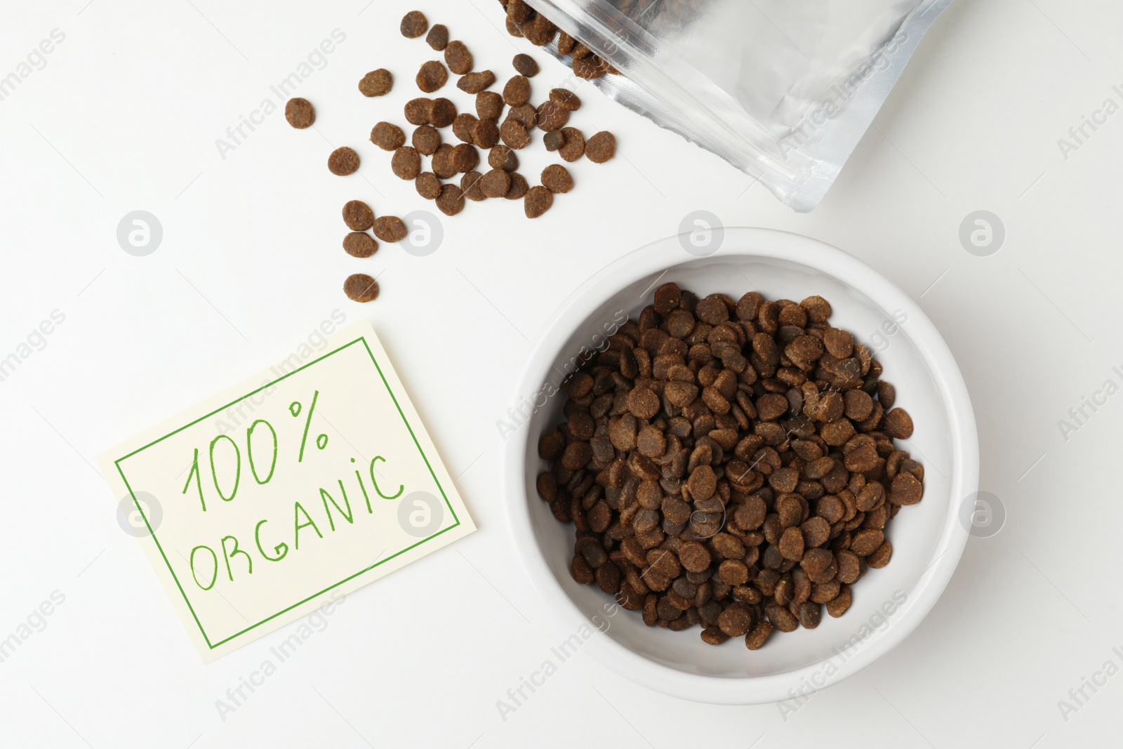 Photo of Pack and feeding bowl of dry cat food with note 100% Organic on white table, flat lay