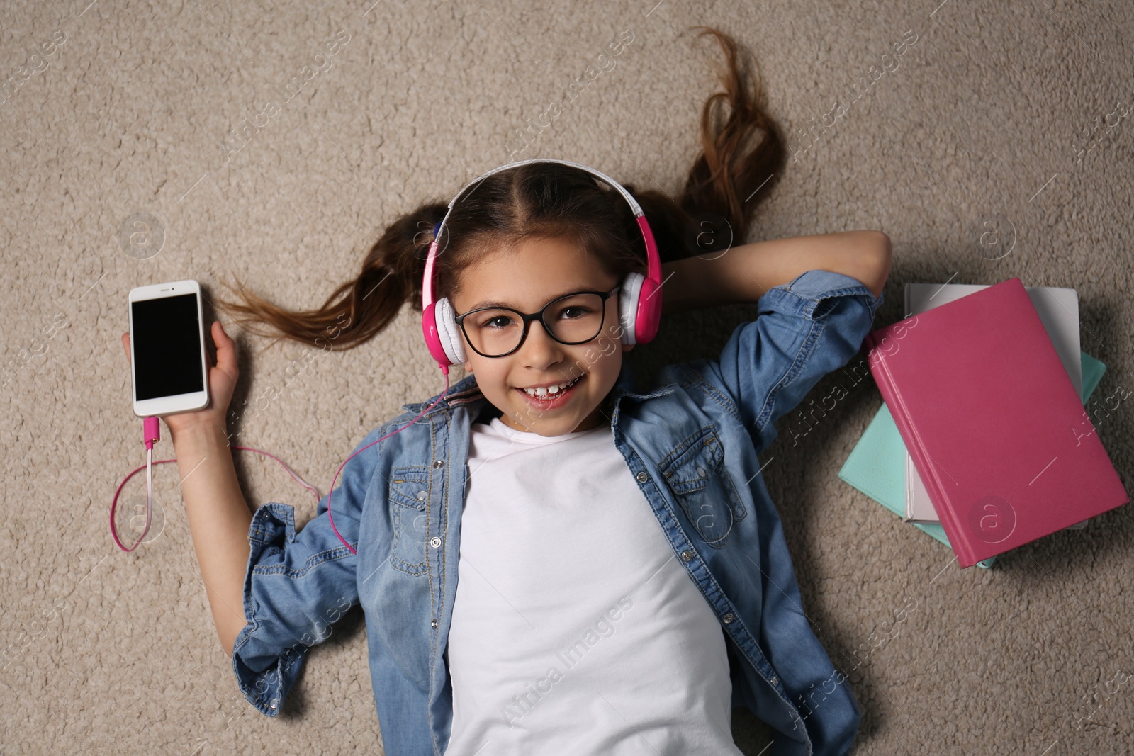 Photo of Cute little girl listening to audiobook on floor, top view