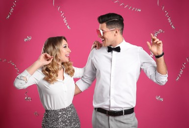 Photo of Happy couple and falling down serpentines on pink background