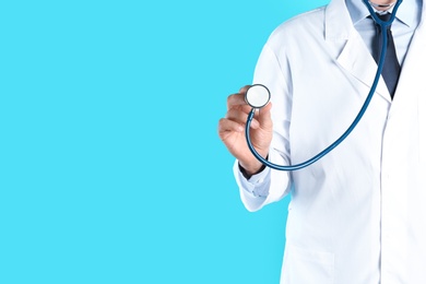 Male doctor holding stethoscope on color background, closeup with space for text