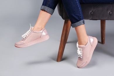 Woman with trendy sport shoes sitting in armchair on grey background