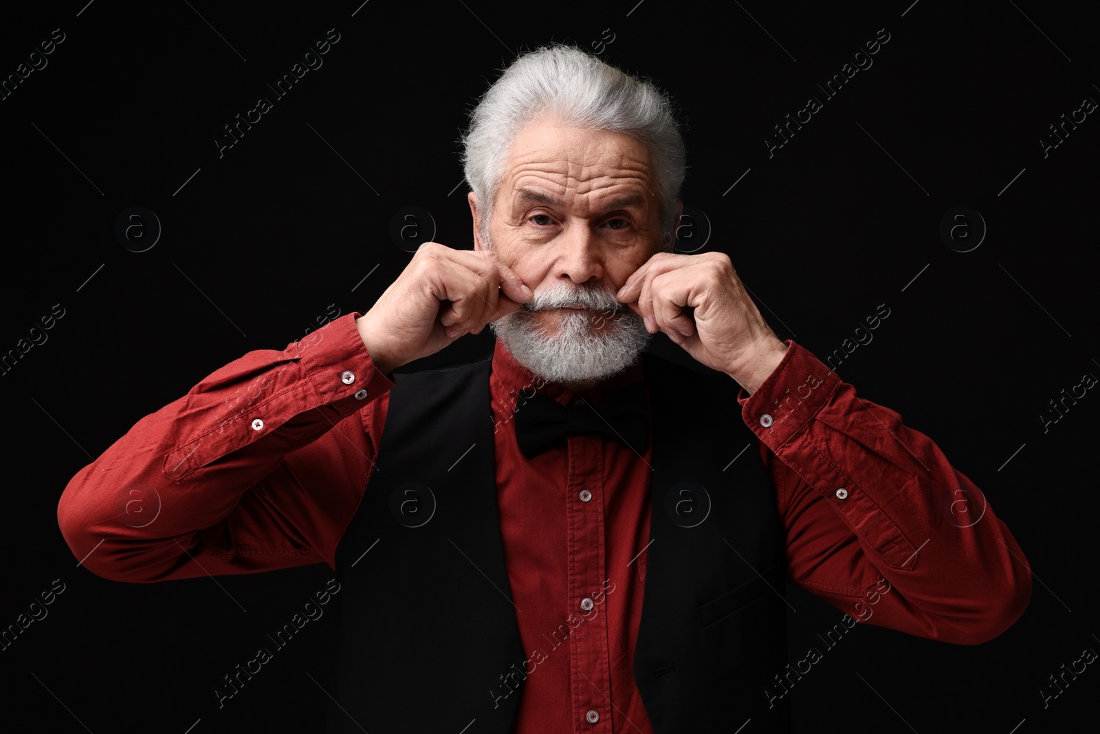 Photo of Senior man touching mustache on black background