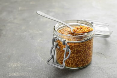 Whole grain mustard in jar and spoon on grey table. Space for text