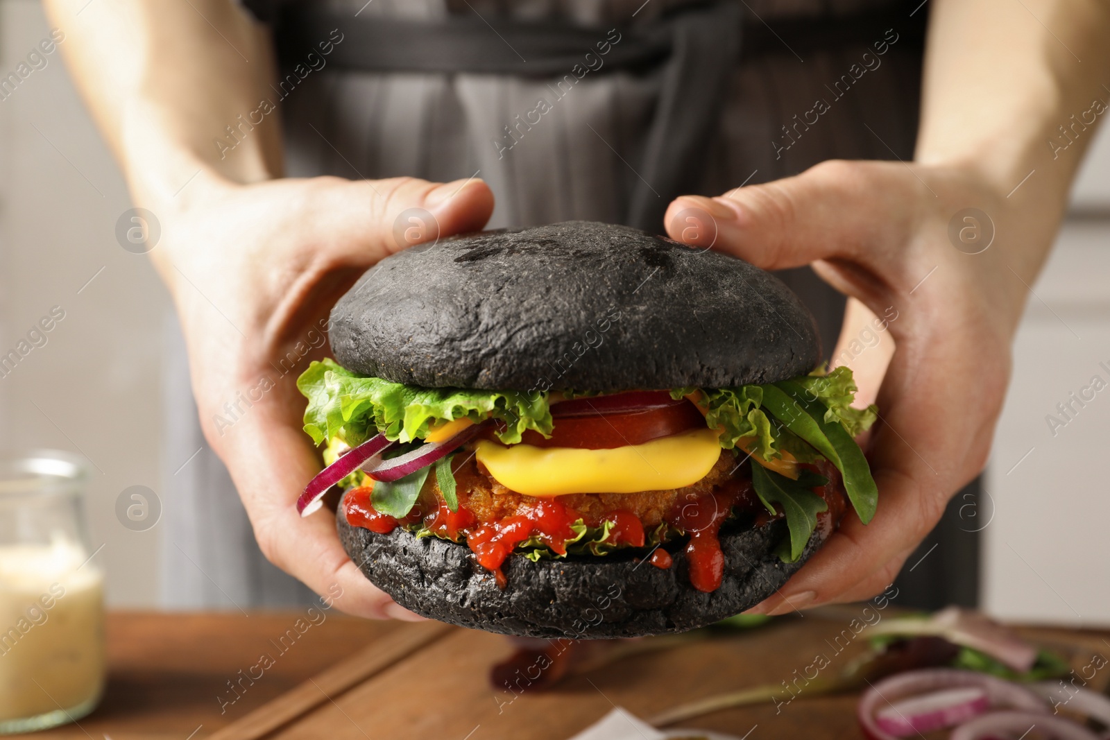 Photo of Woman holding tasty black vegetarian burger over table, closeup