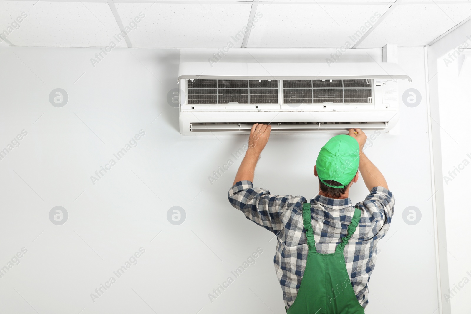 Photo of Male technician fixing modern air conditioner indoors