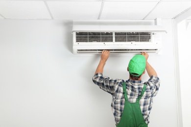 Photo of Male technician fixing modern air conditioner indoors