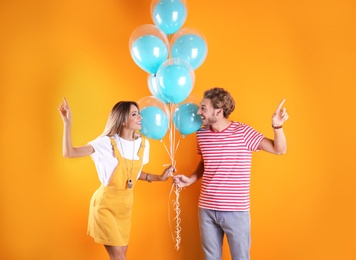 Young couple with air balloons on color background