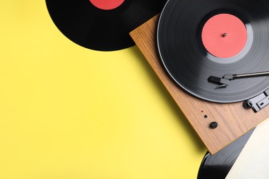 Photo of Modern player and vinyl records on yellow background, flat lay. Space for text