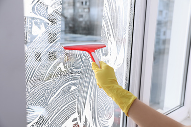 Woman cleaning window with squeegee indoors, closeup