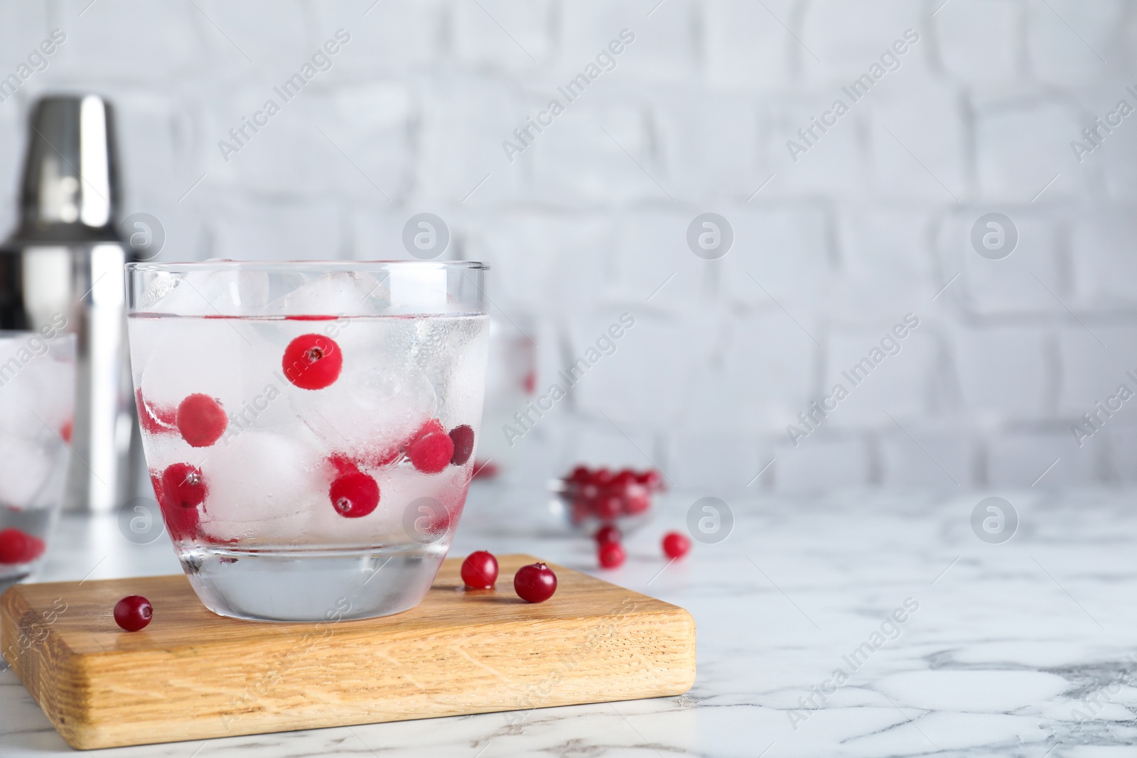 Photo of Glass of cocktail with vodka, ice and cranberry on white marble table. Space for text