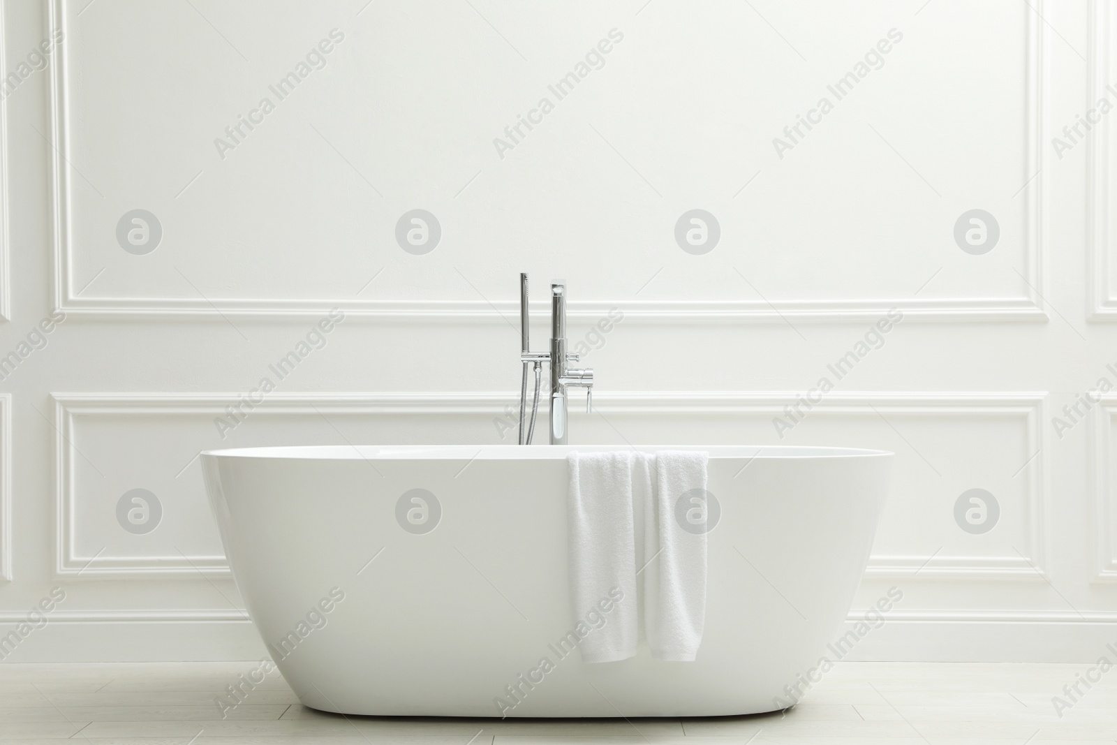 Photo of Modern ceramic bathtub with towel near white wall indoors