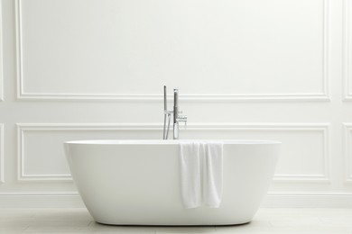 Photo of Modern ceramic bathtub with towel near white wall indoors