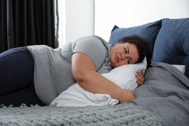 Photo of Depressed overweight woman hugging pillow on bed