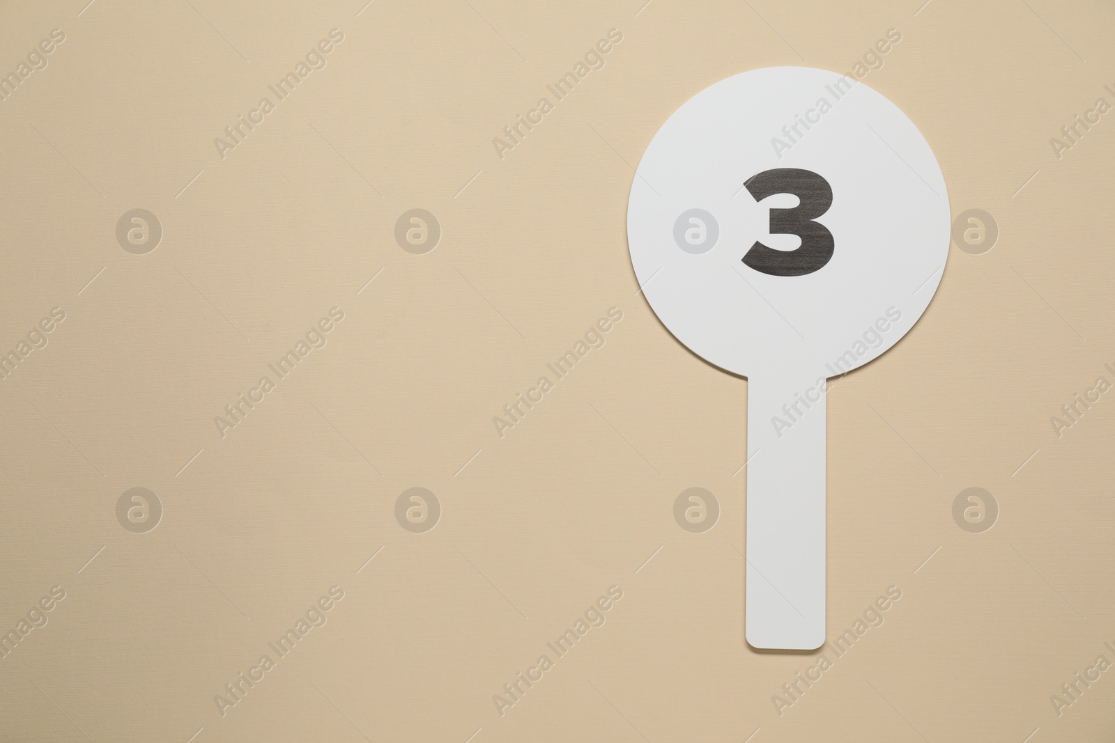 Photo of Auction paddle with number 3 on beige background, top view. Space for text