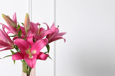 Beautiful pink lily flowers against white wall, closeup. Space for text