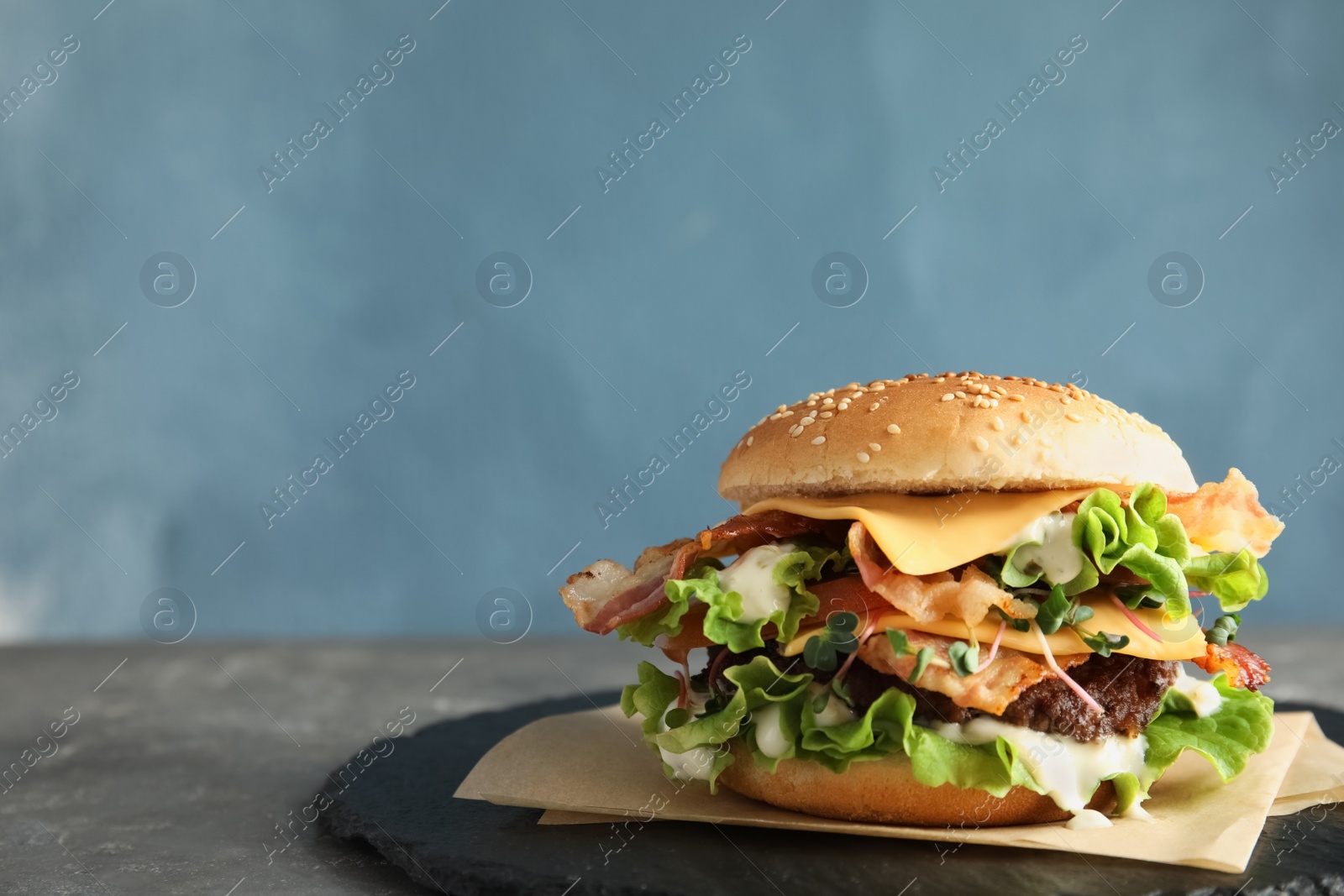 Photo of Tasty burger with bacon on table against color background. Space for text