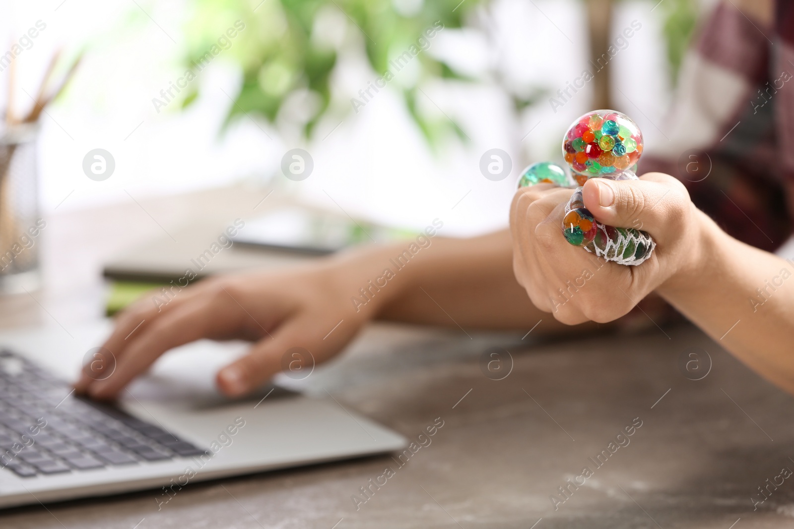 Photo of Woman squeezing colorful slime in office, closeup. Antistress toy