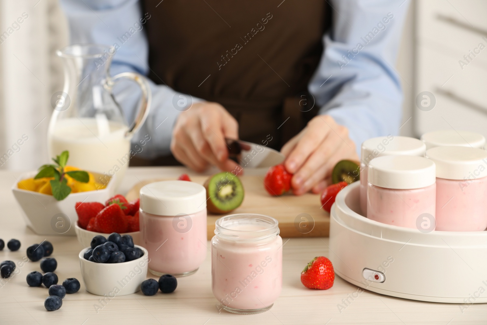 Photo of Woman making tasty yogurt at white wooden table indoors, closeup