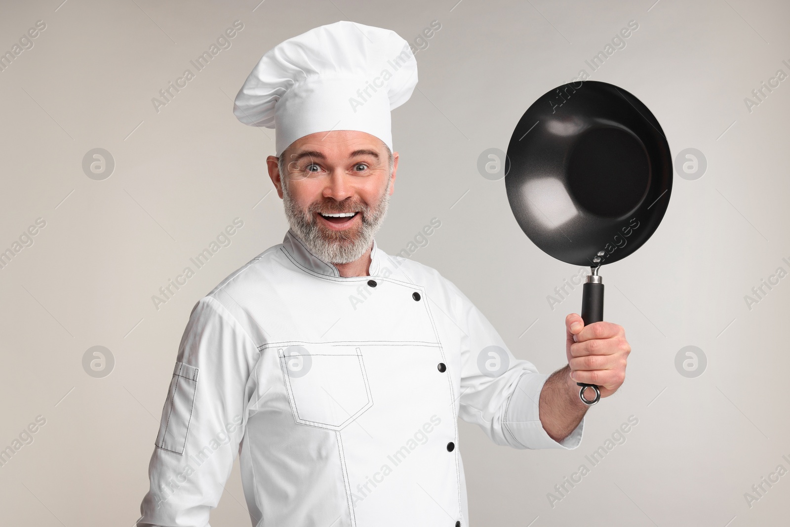 Photo of Emotional chef in uniform holding wok on grey background