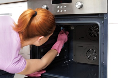 Photo of Woman cleaning modern oven with rag in kitchen